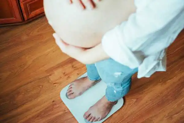 Image of woman weighing herself and experiencing weight gain through pregnancy Edgbaston